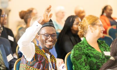 An image of one man in his traditional attire, smiling and raising his hand 